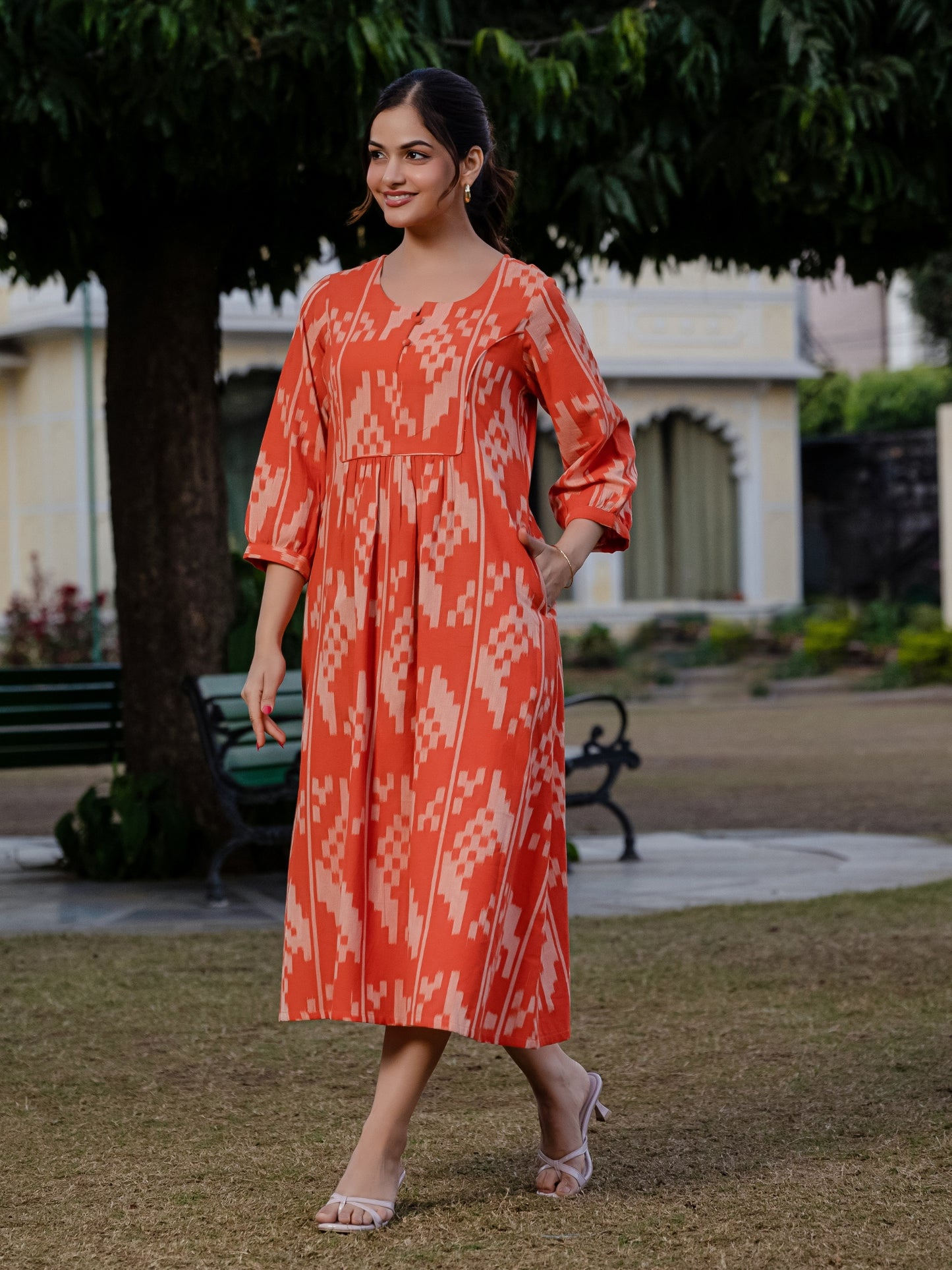 Front view of an orange ikkat cotton dress captured in natural light, with the model posing playfully outdoors.