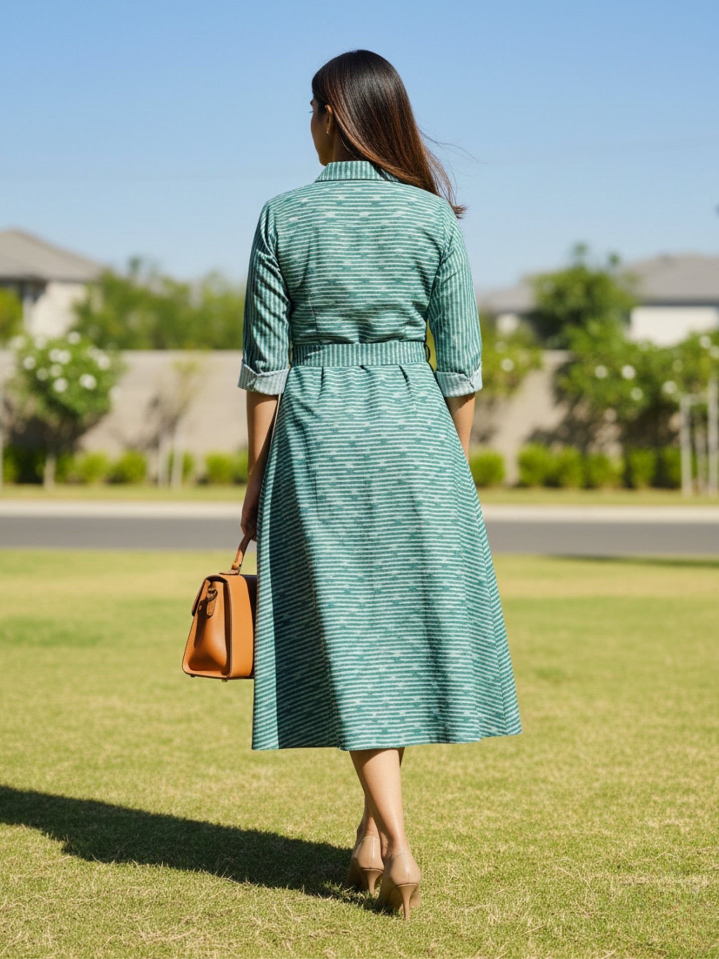 Back view of calf-length handwoven ikat dress with belt detail and clean silhouette, displayed on model outdoors.